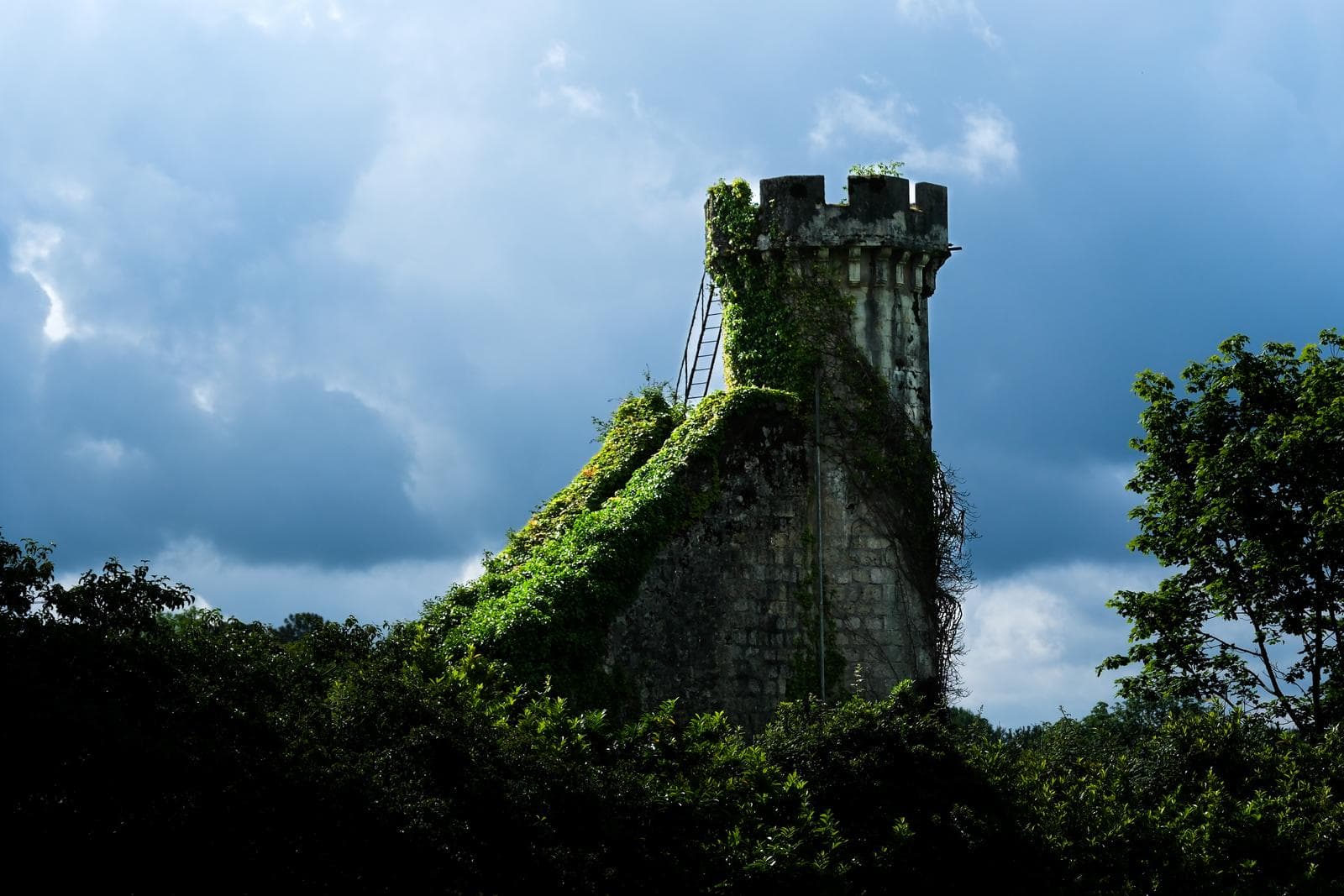 Tour de pierre envahie de lierre sous un ciel d’orage