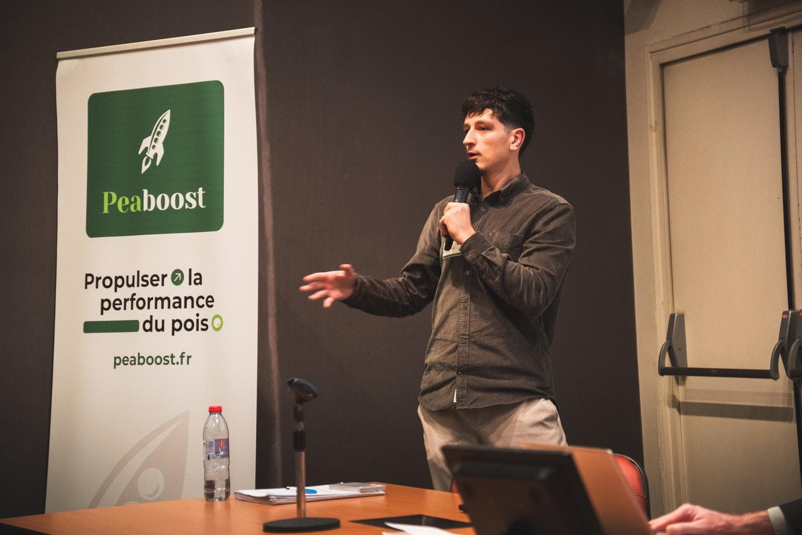Intervenant au micro devant le kakémono Peaboost