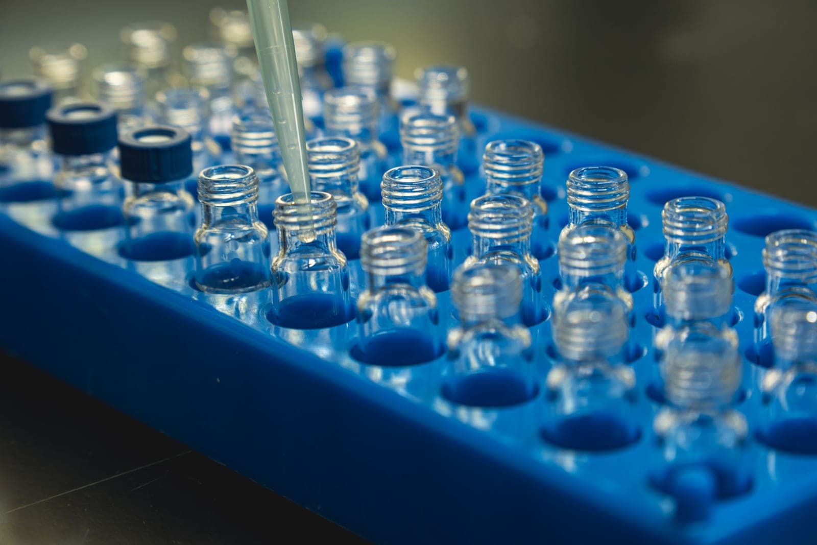 Rangées de flacons en verre sur un portoir bleu, une pipette au-dessus